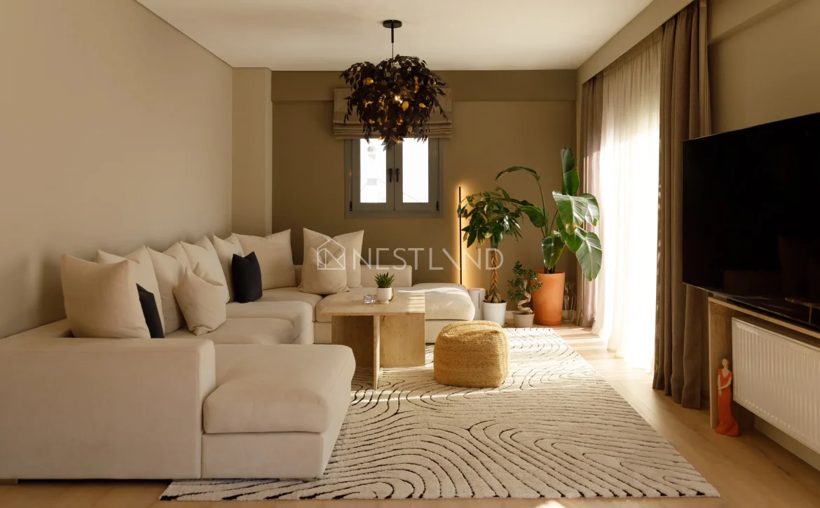 A cozy living room with beige sofa, patterned rug, plants, and a unique chandelier.