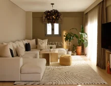 A cozy living room with beige sofa, patterned rug, plants, and a unique chandelier.