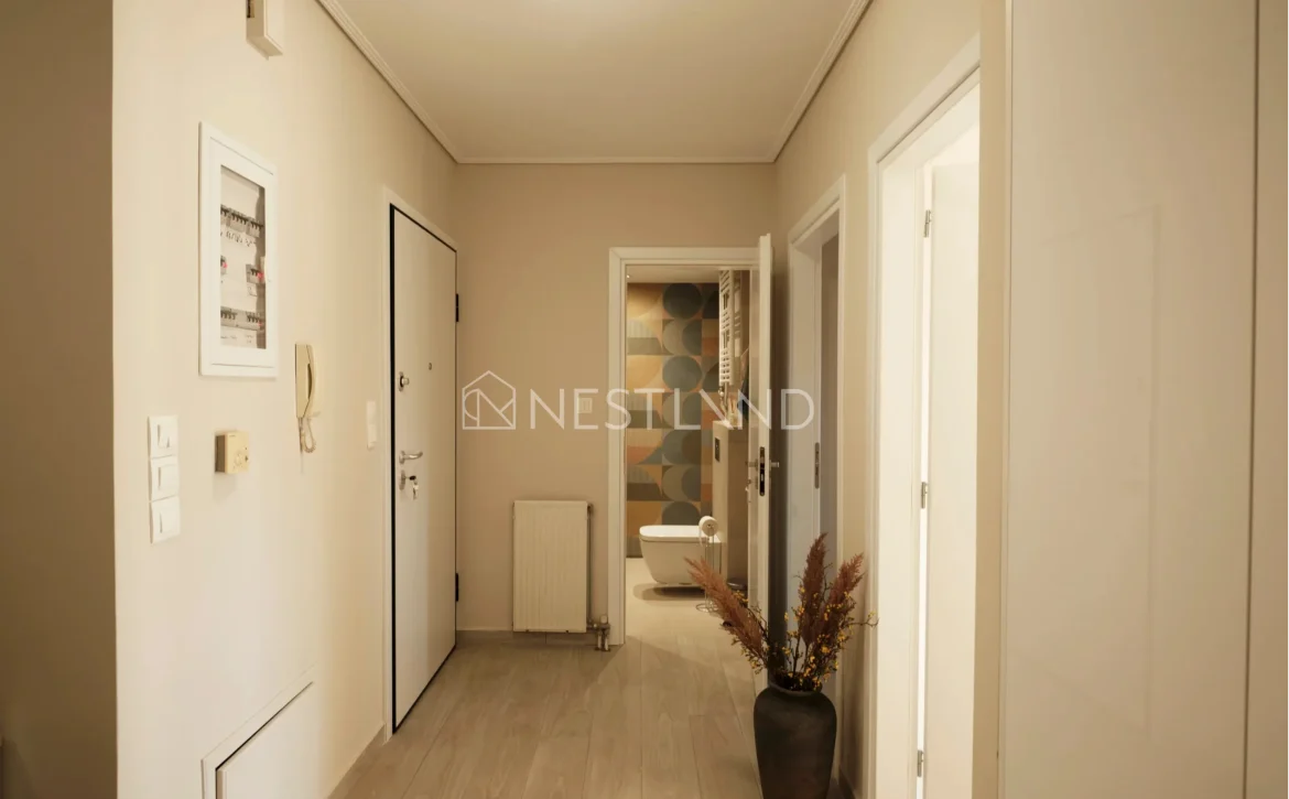 A warm-lit hallway with wooden flooring, white doors, and decorative framed pictures on the walls.