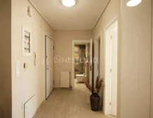 A warm-lit hallway with wooden flooring, white doors, and decorative framed pictures on the walls.