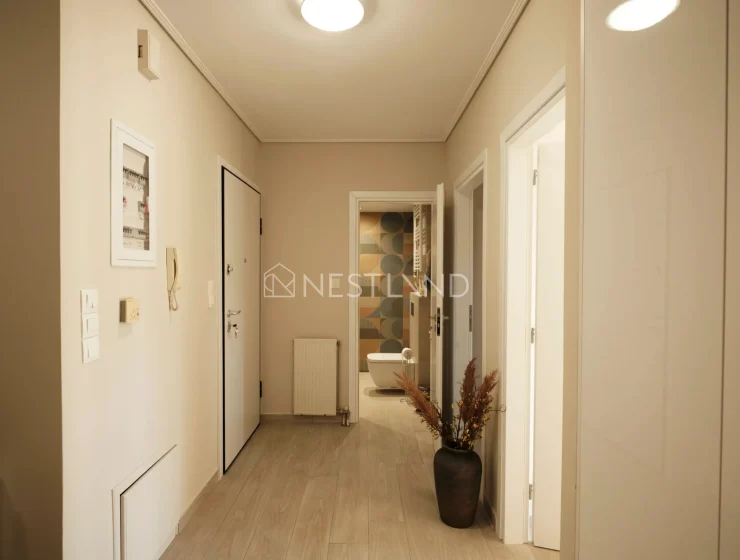 A warm-lit hallway with wooden flooring, white doors, and decorative framed pictures on the walls.