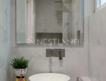 A modern bathroom with marble walls, a white basin, and a decorative plant pot.