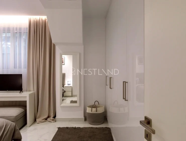 Elegant minimalistic bedroom with a TV, neutral tones, and sheer curtains.