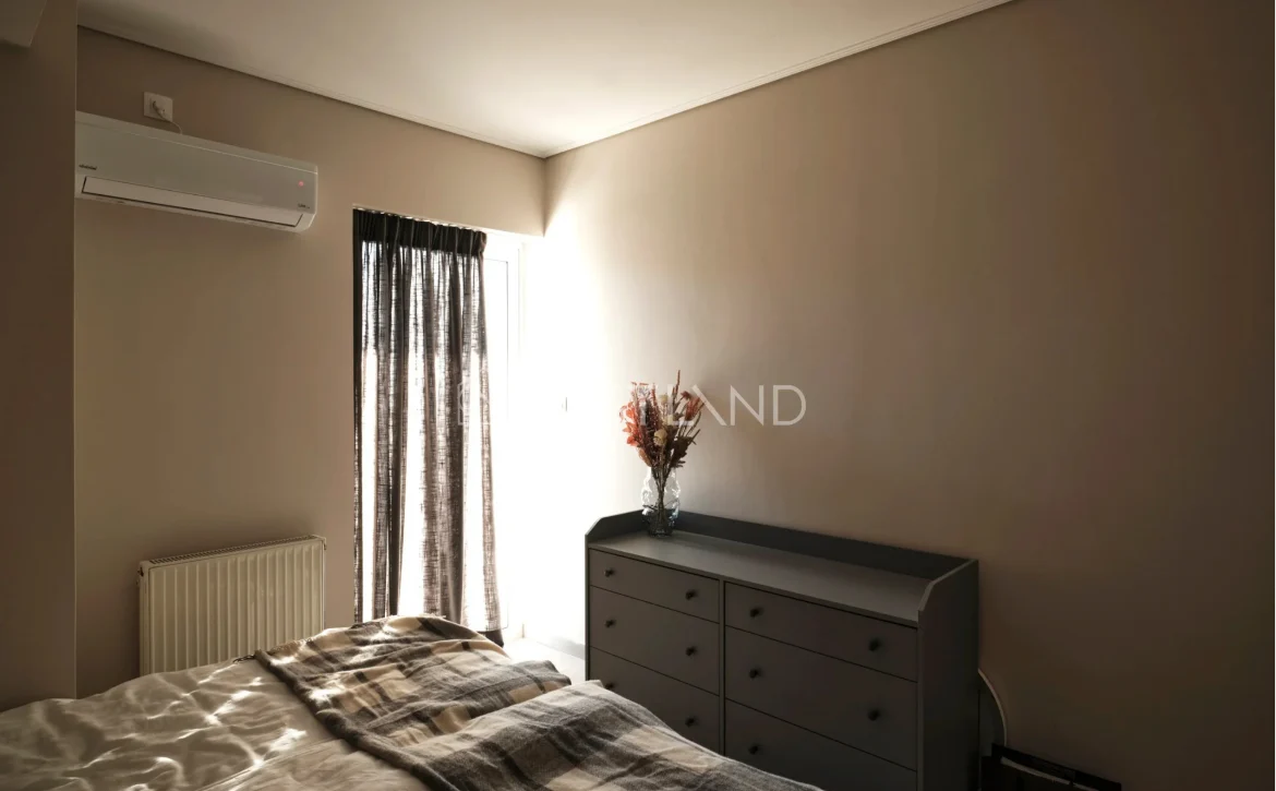 A minimalist bedroom with beige walls, a bed with checkered blanket, a grey dresser, and curtains.