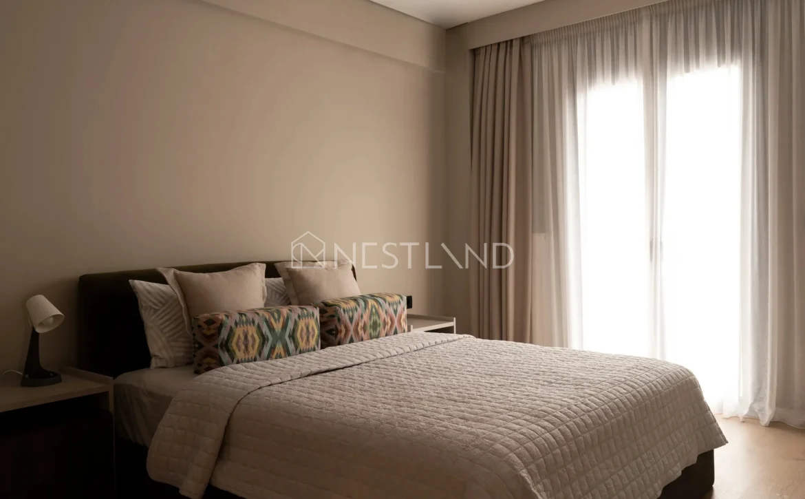 Modern bedroom with a neatly made bed, patterned pillows, and sheer curtains diffusing sunlight.