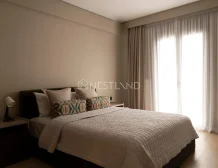 Modern bedroom with a neatly made bed, patterned pillows, and sheer curtains diffusing sunlight.