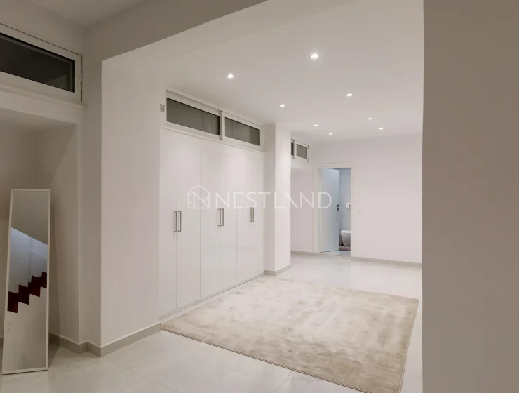Modern hallway with white cabinetry, a mirror, and a beige rug on a tiled floor.