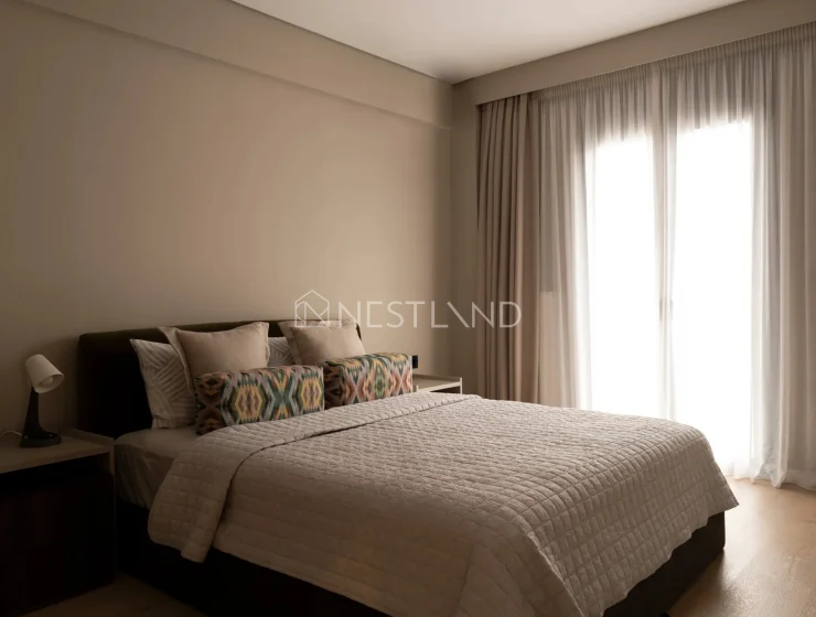 Modern bedroom with a neatly made bed, patterned pillows, and sheer curtains diffusing sunlight.