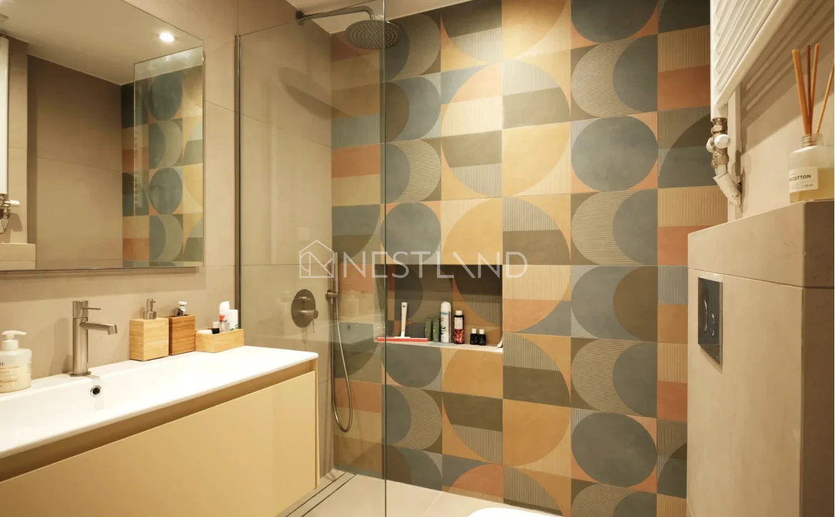 Modern bathroom with geometric tiled walls, glass shower, and vanity area.
