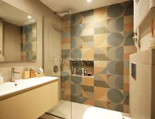 Modern bathroom with geometric tiled walls, glass shower, and vanity area.