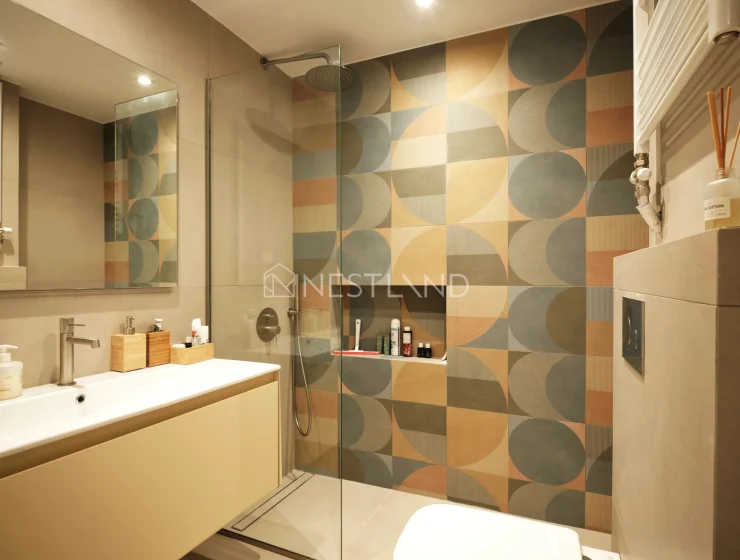 Modern bathroom with geometric tiled walls, glass shower, and vanity area.