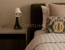 Cozy bedroom corner with a stylish lamp on a nightstand, plush headboard, and patterned pillows.