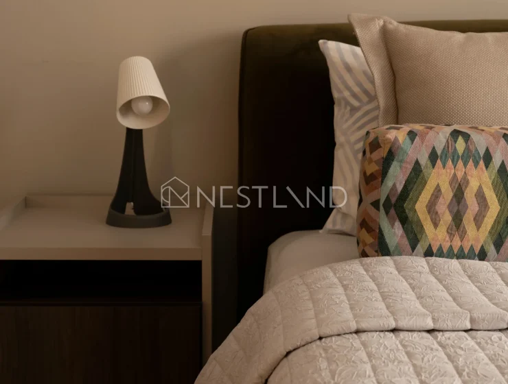 Cozy bedroom corner with a stylish lamp on a nightstand, plush headboard, and patterned pillows.