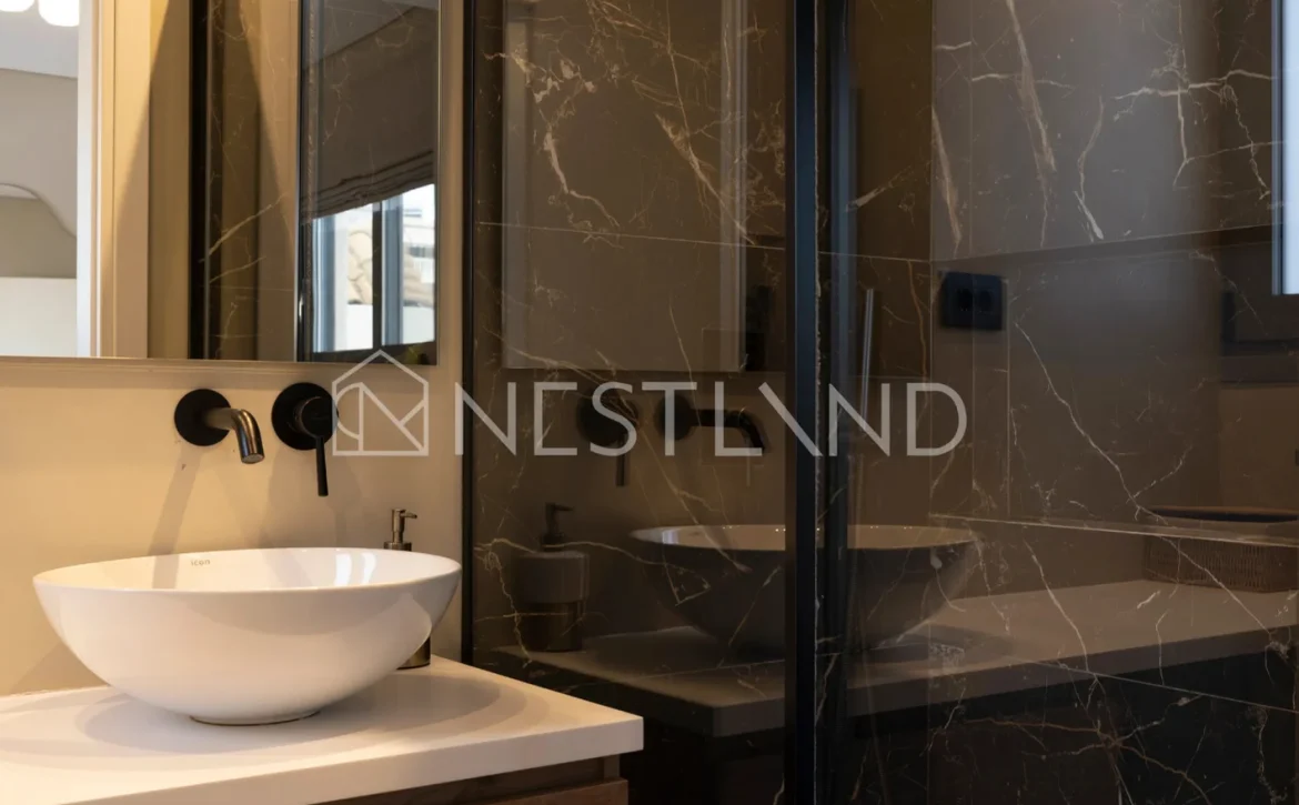 Modern bathroom with black marble walls, glass shower, and white vessel sink on wooden vanity.