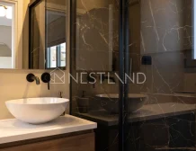 Modern bathroom with black marble walls, glass shower, and white vessel sink on wooden vanity.