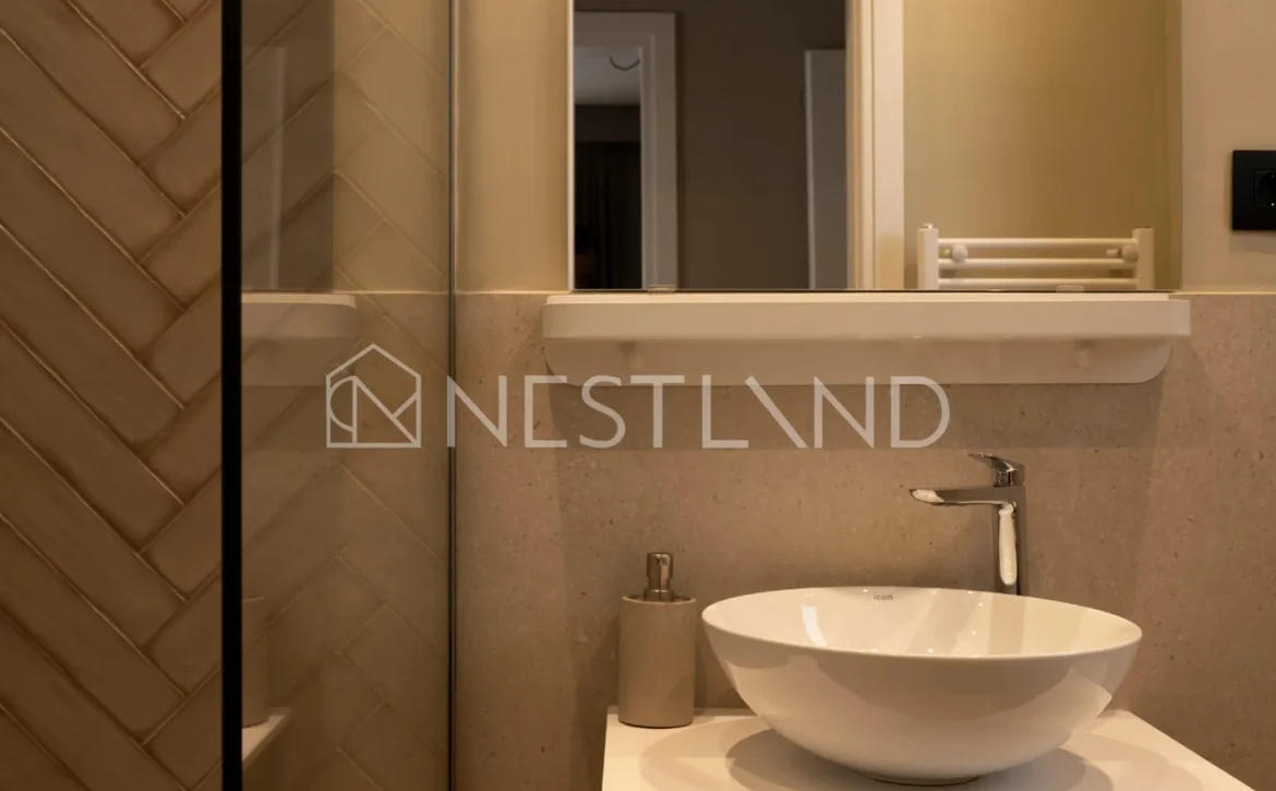 Modern bathroom vanity with a white vessel sink, wooden cabinet, and mirror, featuring herringbone tile wall.