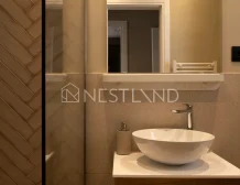 Modern bathroom vanity with a white vessel sink, wooden cabinet, and mirror, featuring herringbone tile wall.