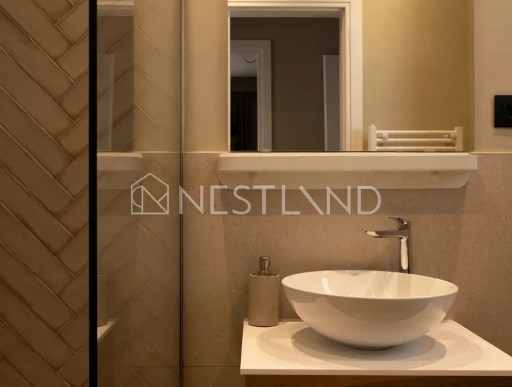 Modern bathroom vanity with a white vessel sink, wooden cabinet, and mirror, featuring herringbone tile wall.