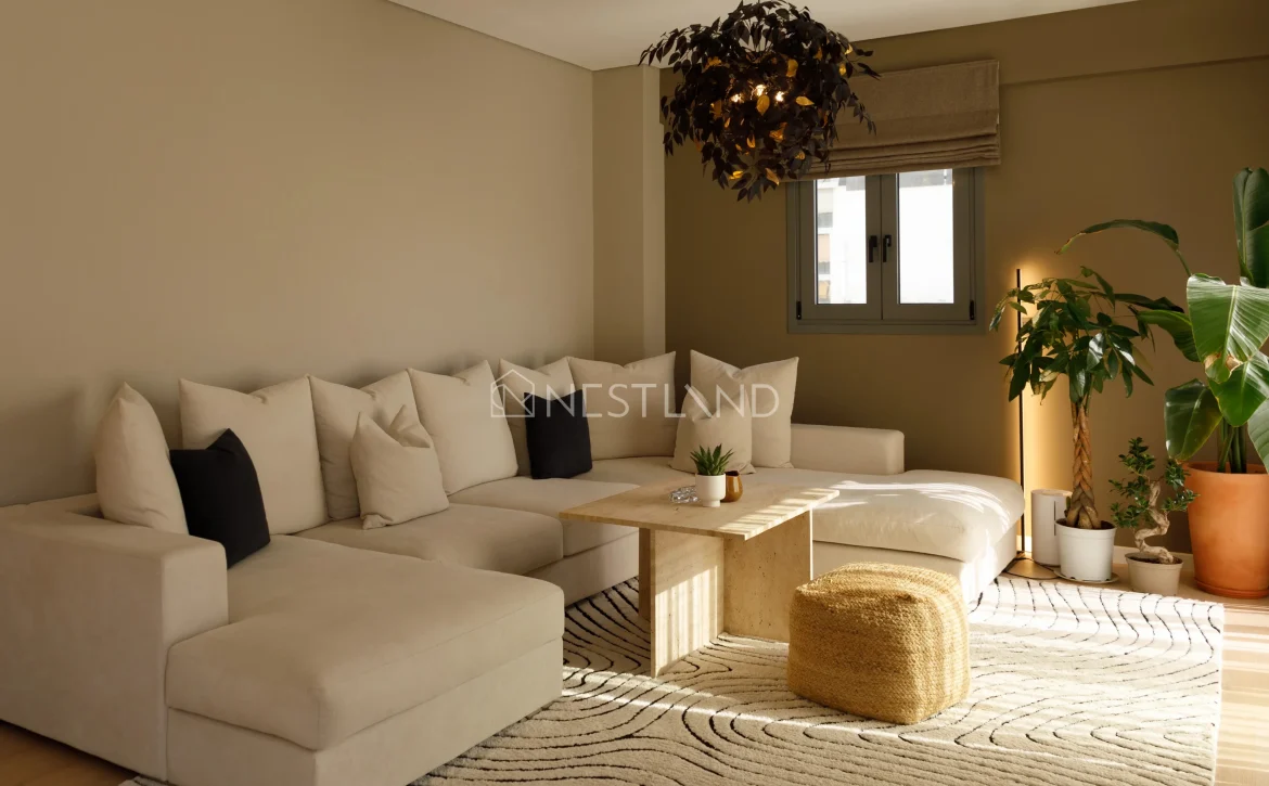 Modern living room with sectional sofa, wooden table, patterned rug, and indoor plants.