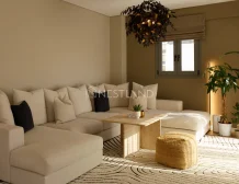 Modern living room with sectional sofa, wooden table, patterned rug, and indoor plants.