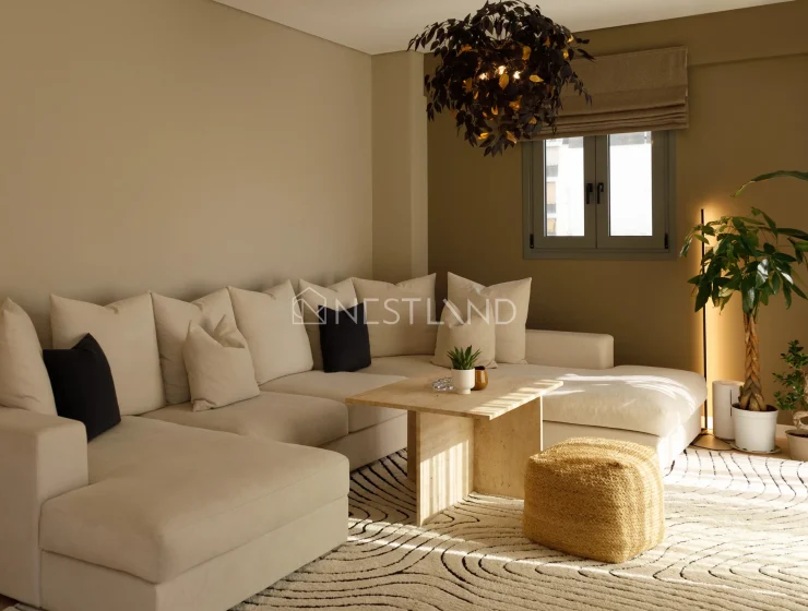 Modern living room with sectional sofa, wooden table, patterned rug, and indoor plants.