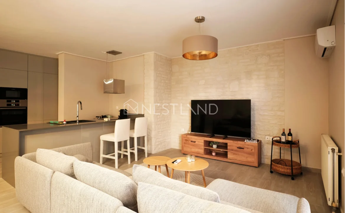 Modern living room with sofa set, TV, kitchen area, and stone accent wall.