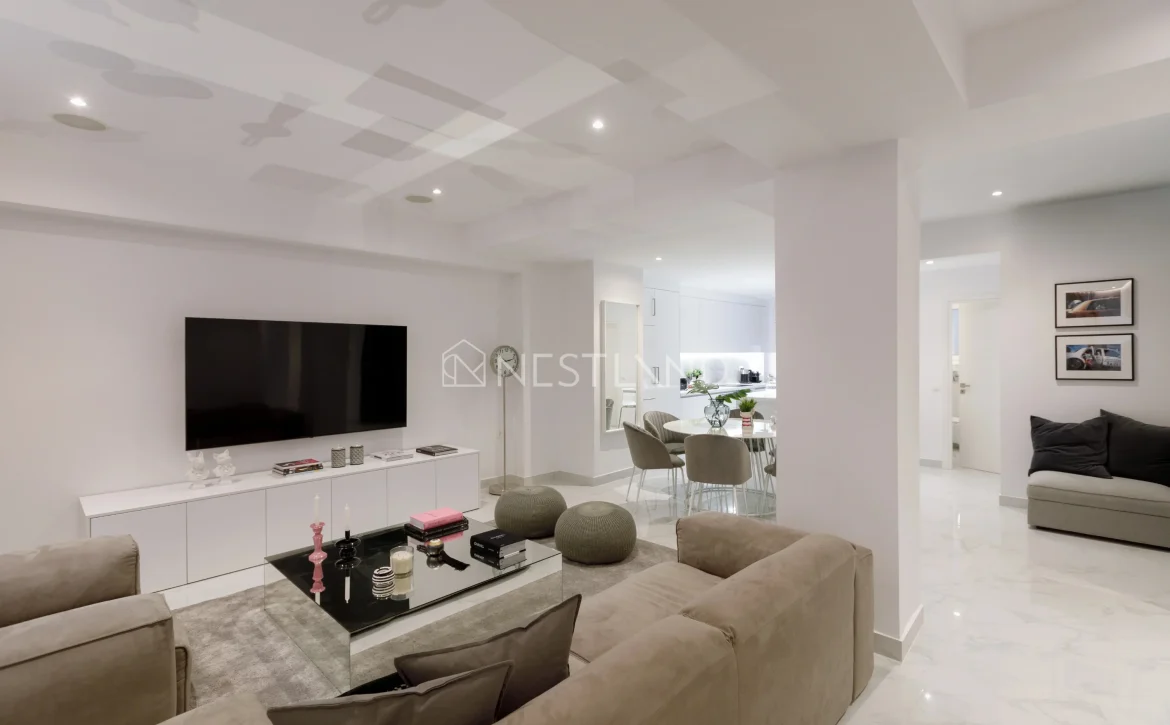 Modern living room with white furniture, marble floor, and dining area in the background.