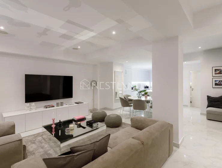 Modern living room with white furniture, marble floor, and dining area in the background.