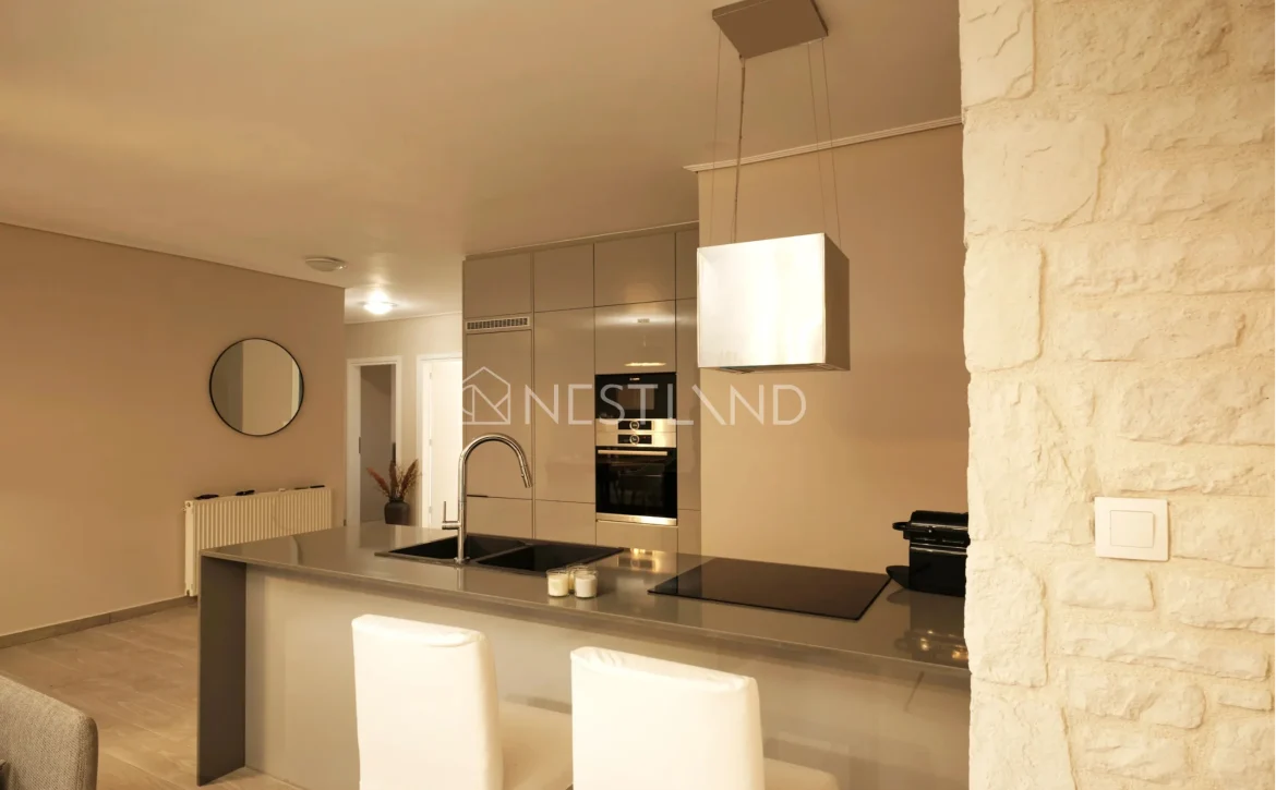 Modern kitchen interior with beige cabinets, built-in appliances, and a breakfast bar with stools.