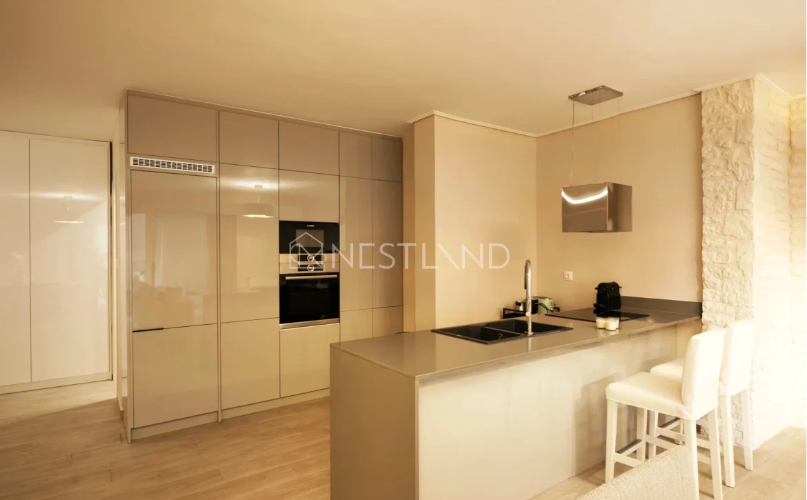 Modern kitchen interior with beige cabinets, built-in appliances, and a breakfast bar with stools.