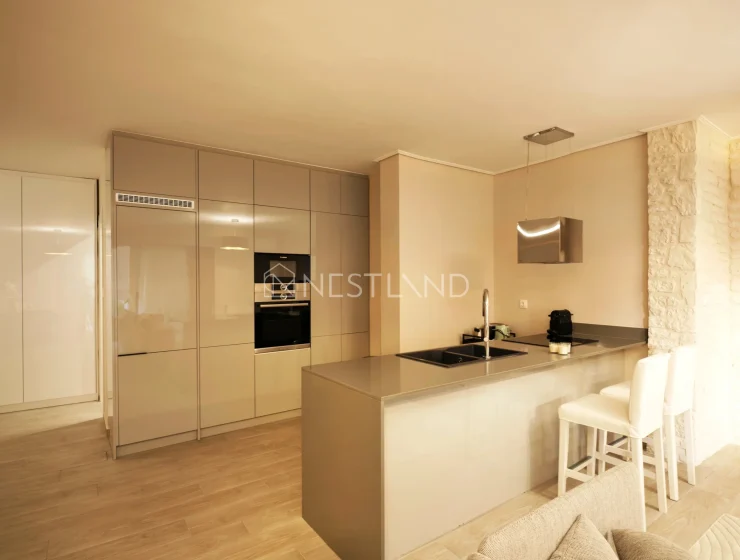 Modern kitchen interior with beige cabinets, built-in appliances, and a breakfast bar with stools.