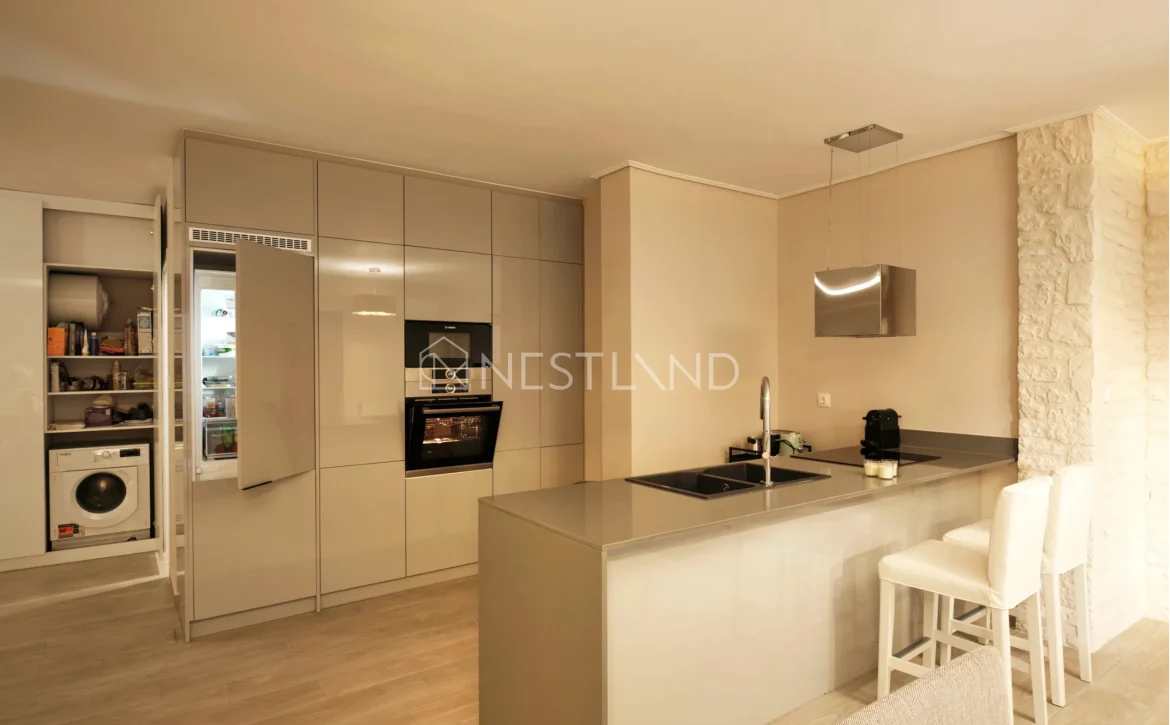 Modern kitchen with beige cabinets, integrated appliances, and a breakfast bar with stools.