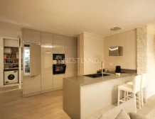 Modern kitchen with beige cabinets, integrated appliances, and a breakfast bar with stools.