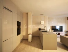 Modern kitchen with white cabinets, built-in appliances, and an island, adjacent to a living area with a stone wall.