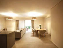 Modern living and dining area with beige tones, sofa, table, and open balcony door.