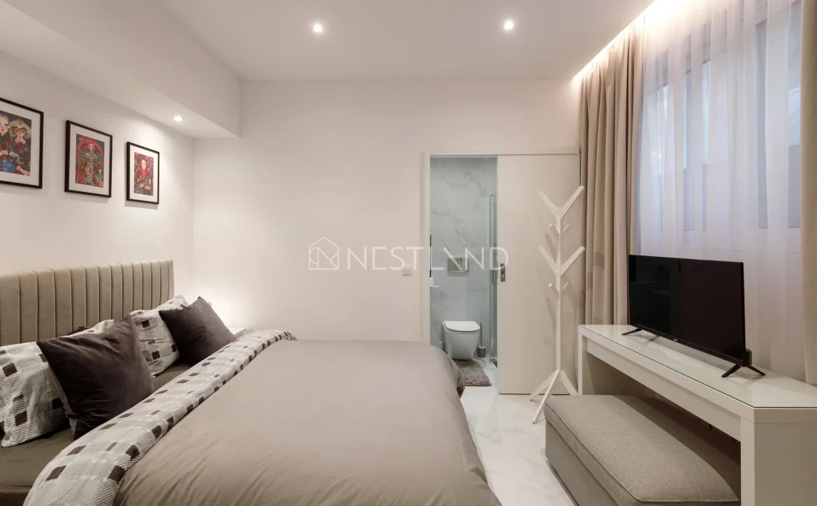 Modern bedroom with a large bed, artwork on the wall, TV, and an en-suite bathroom.