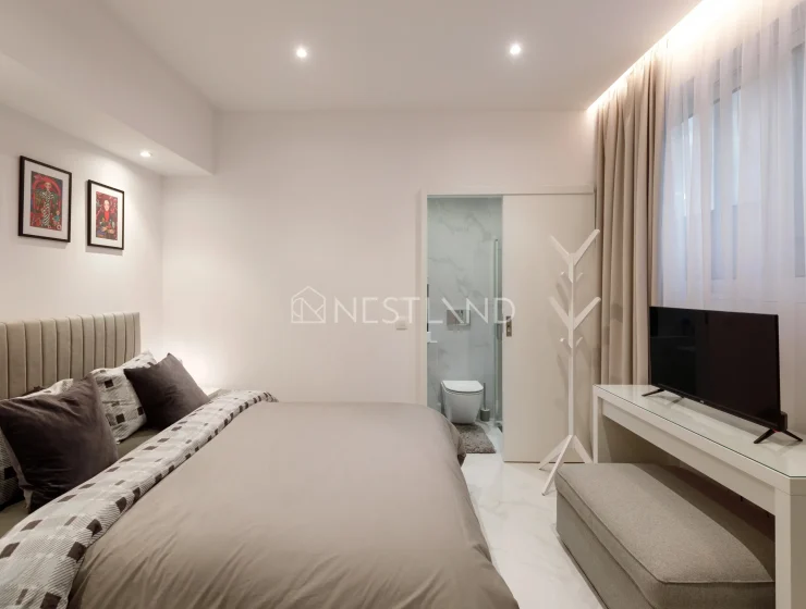 Modern bedroom with a large bed, artwork on the wall, TV, and an en-suite bathroom.