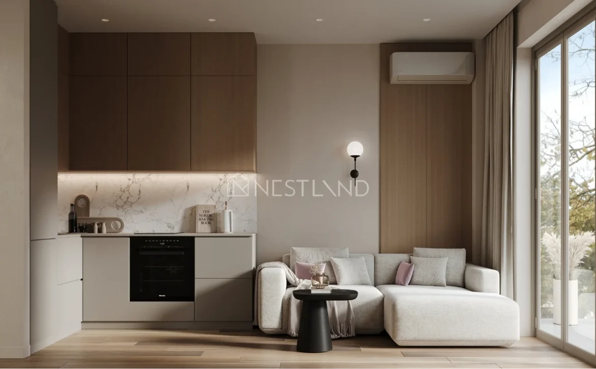 Modern living room with kitchenette, sofa, and large window overlooking trees.