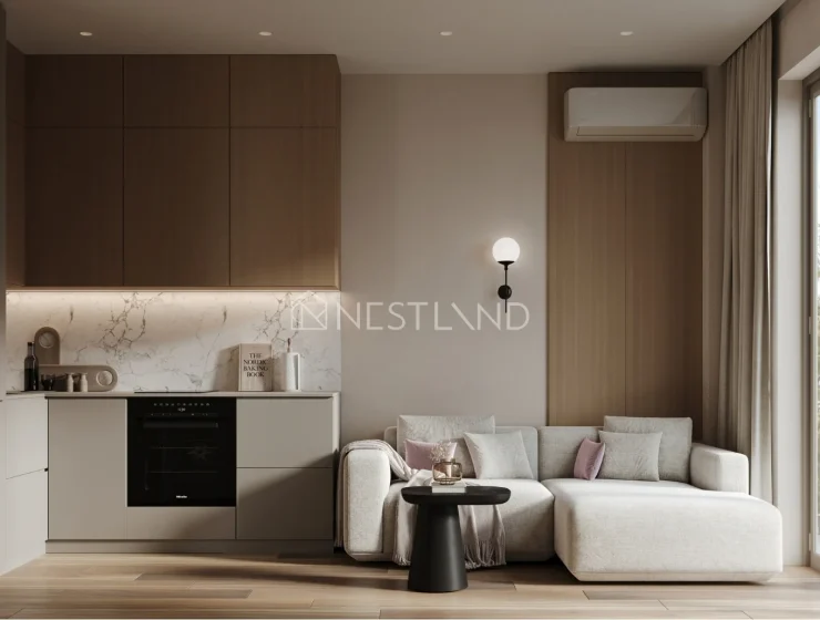 Modern living room with kitchenette, sofa, and large window overlooking trees.