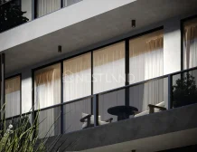Modern apartment balcony with glass doors, curtains, and outdoor furniture.